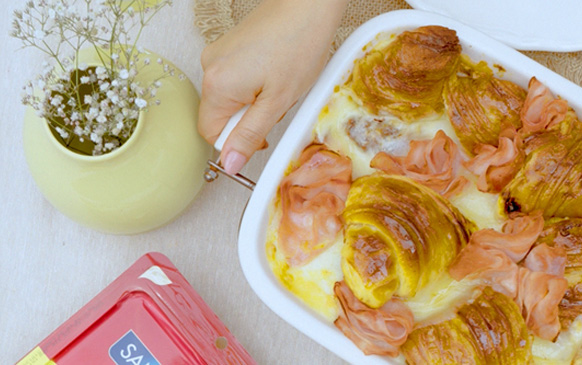 Cazuela horneada de croissants dorados con queso derretido y jamón real de pierna San Rafael, servida en fuente blanca.